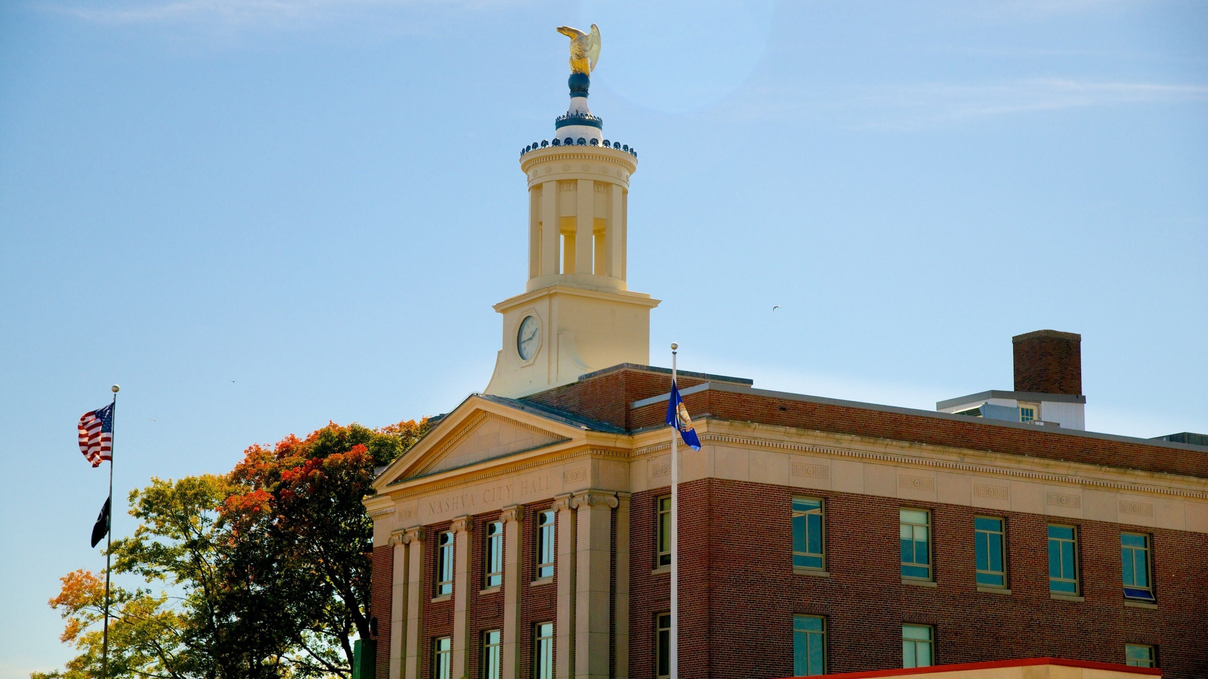 A historic building with a clock tower, American flags, and a statue.