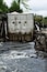 A concrete dam with graffiti, a turbulent river, and a rocky outcrop.