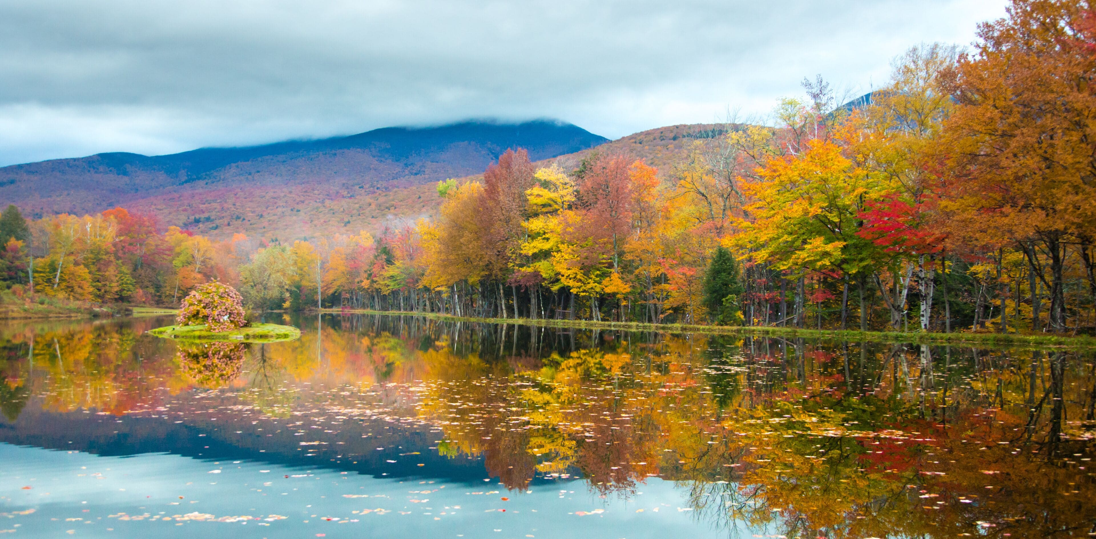 A hardwood forest at peak fall color reflects in Shadow Lake, north of Lincoln, New Hampshire, White Mountain National Forest.