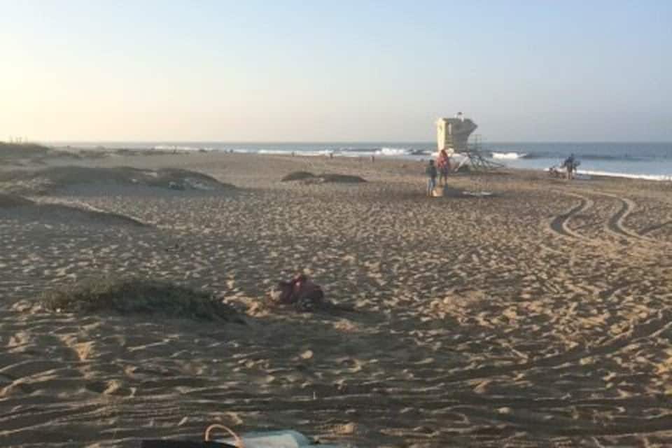 A sandy beach with footprints and a surfboard.