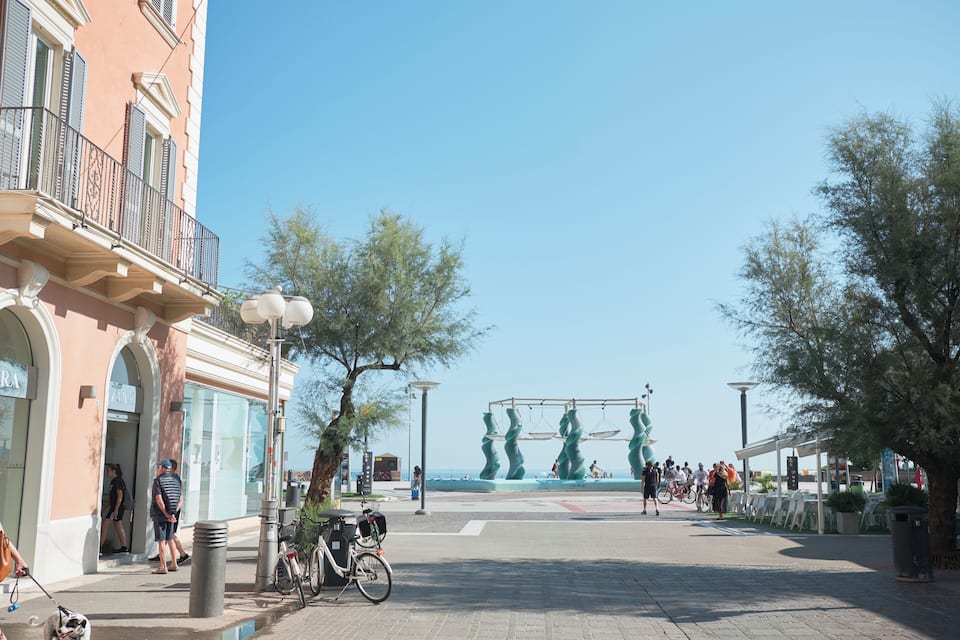 A sunny urban square with a fountain, a dog on a leash, and a bicycle.