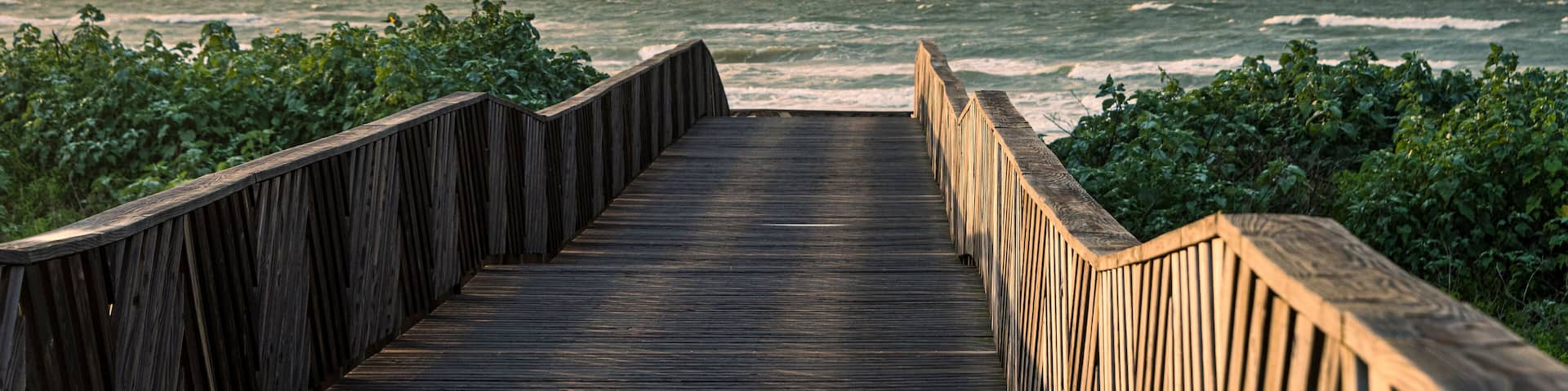 Pasarela de madera que conduce al océano, con olas rompiendo al fondo.