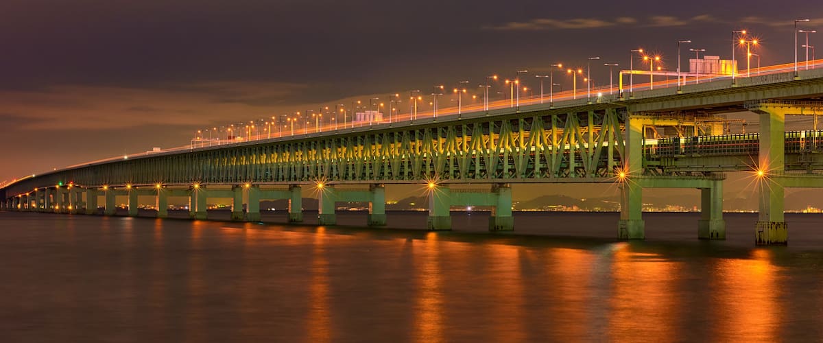 A long bridge with multiple lanes and streetlights, spanning over a body of water.