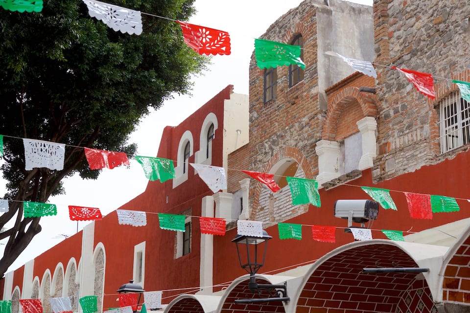 Un edificio con paredes de ladrillo rojo y ventanas arqueadas, decorado con banderas de papel verde y rojo.