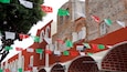 Un edificio con paredes de ladrillo rojo y ventanas arqueadas, decorado con banderas de papel verde y rojo.