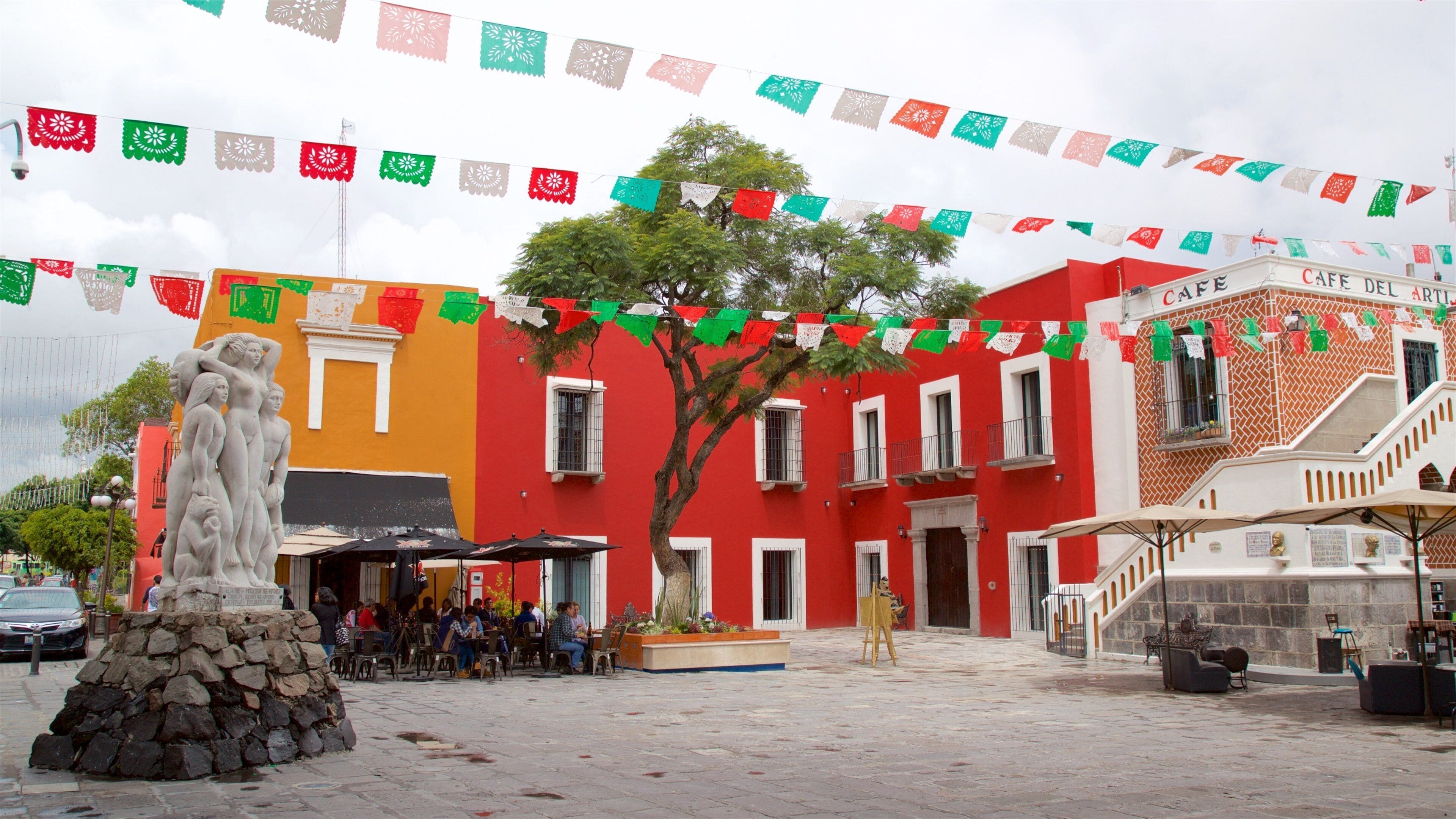A plaza with colorful buildings, a stone statue, and a tree.