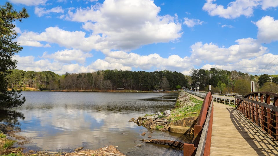 A wooden bridge over a calm lake with trees in the background.