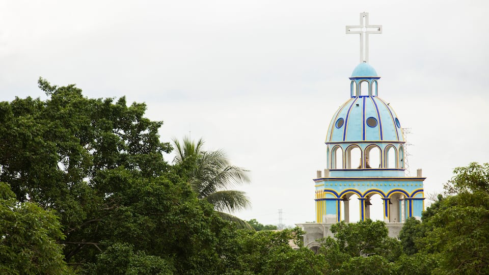 Igreja com cúpula azul e cruz no topo, cercada por árvores.