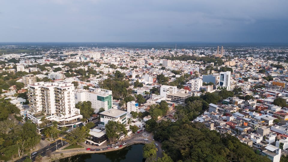 Paisagem urbana densamente povoada, com mistura de edifícios modernos e antigos, uma torre de igreja em destaque, e uma massa d'água em primeiro plano.