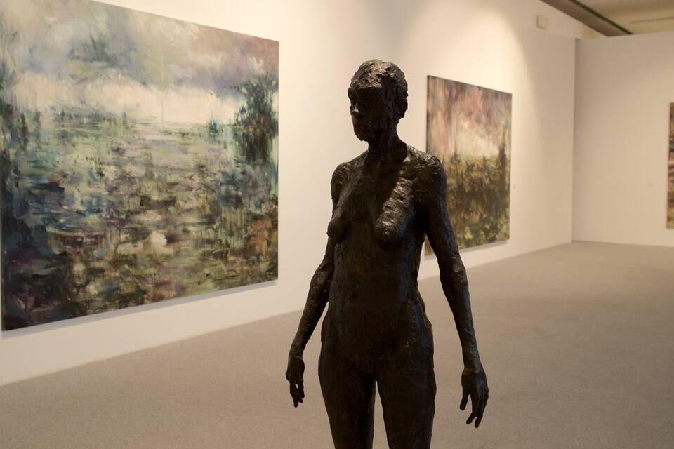 Uma escultura em uma galeria de arte, com pinturas abstratas nas paredes.