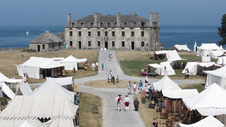A historic stone building with a paved pathway leading to it, surrounded by white tents and people.