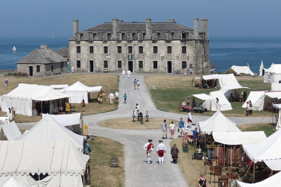 A historic stone building with a paved pathway leading to it, surrounded by white tents and people.