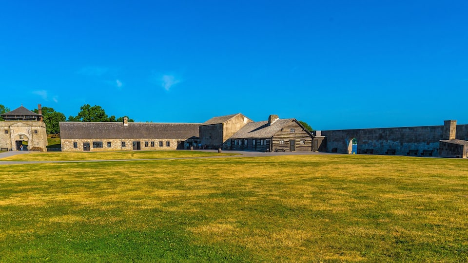 A historic building complex with a large lawn, stone structures, and a clear blue sky.