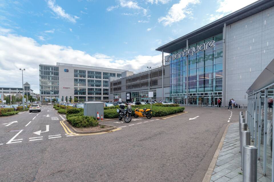 A modern building with a glass facade and the name "Union Square" on it. There are motorcycles parked in front, and a road with directional arrows.
