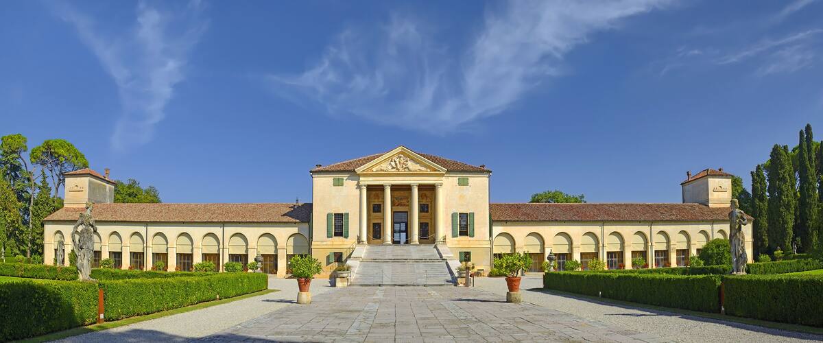 A classical building with a central entrance, flanked by symmetrical wings and a manicured garden.