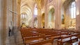 A cathedral interior with high vaulted ceilings, rows of wooden pews, stained glass windows, and a large altar.