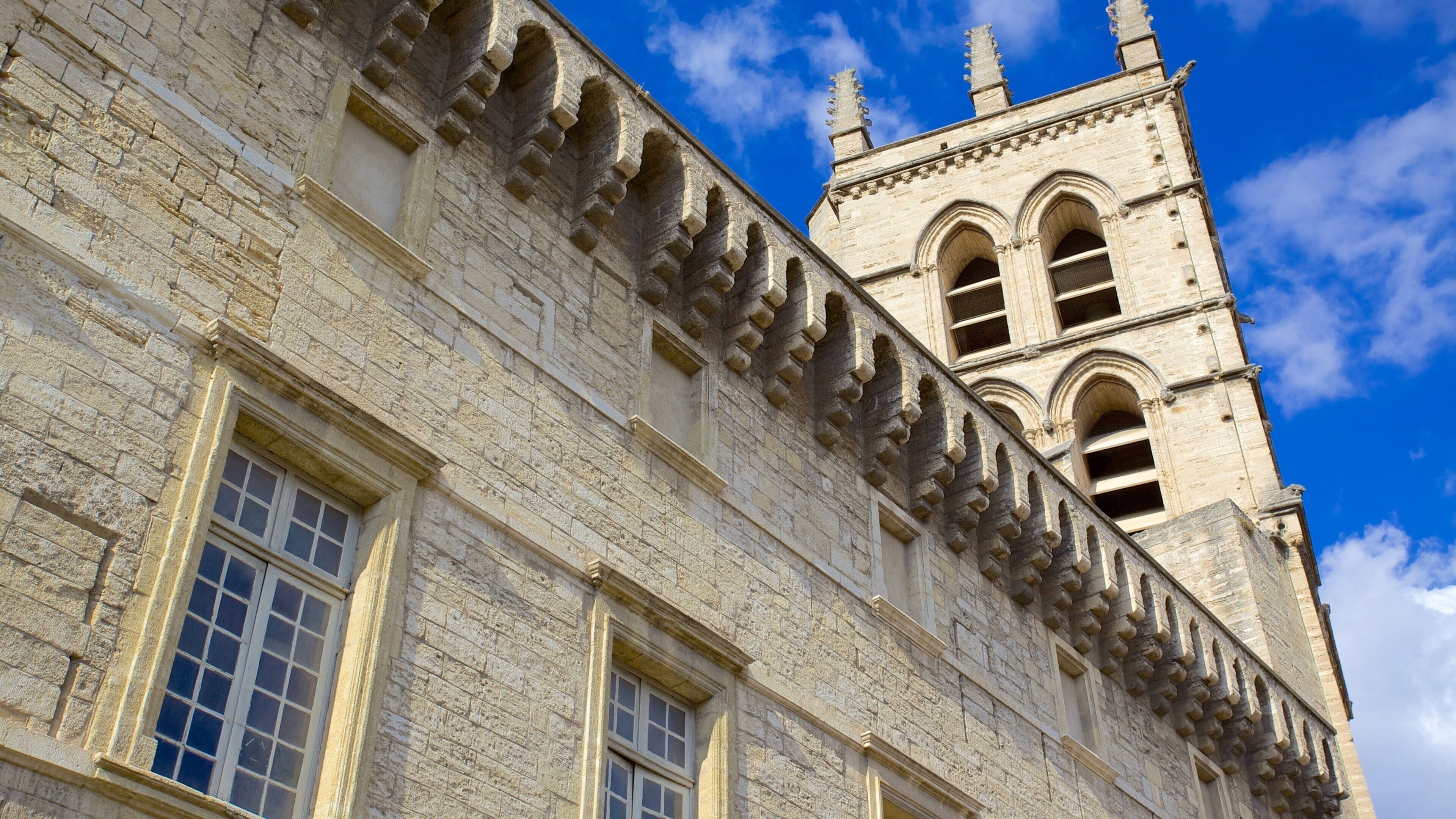 A historic stone building with arched windows and a tall tower with a spire.