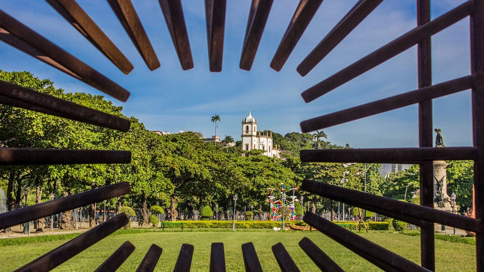 Um parque com vista para uma igreja branca e um campanário, cercado por árvores e vegetação.