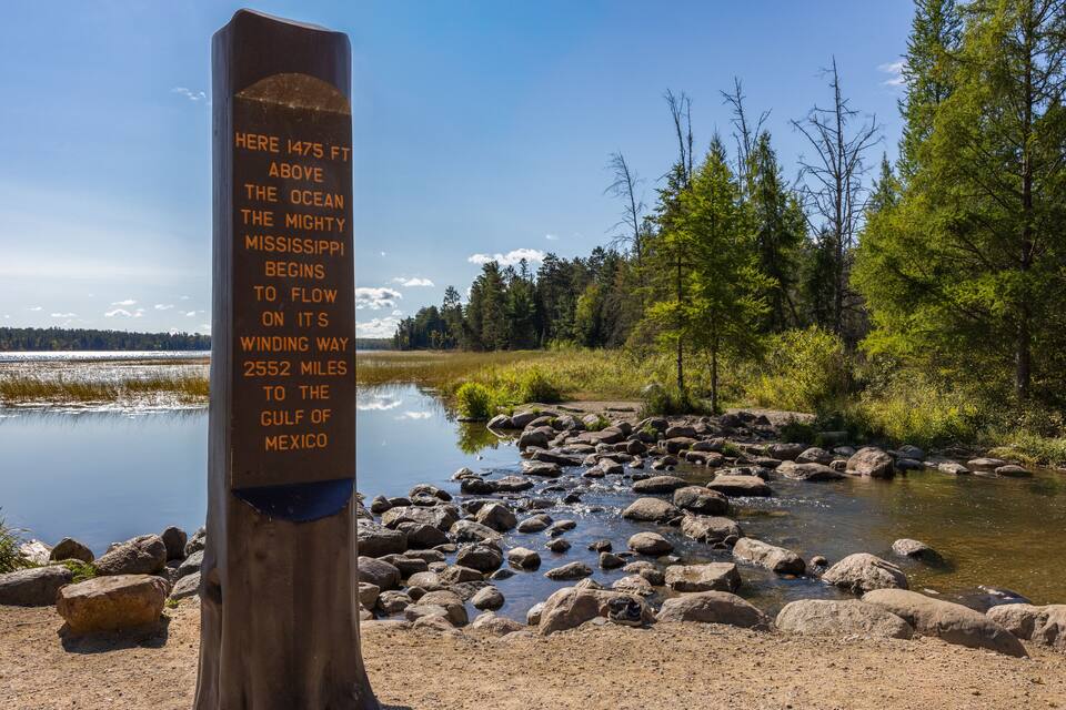 A wooden sign by a river with text about the Mississippi River's flow.