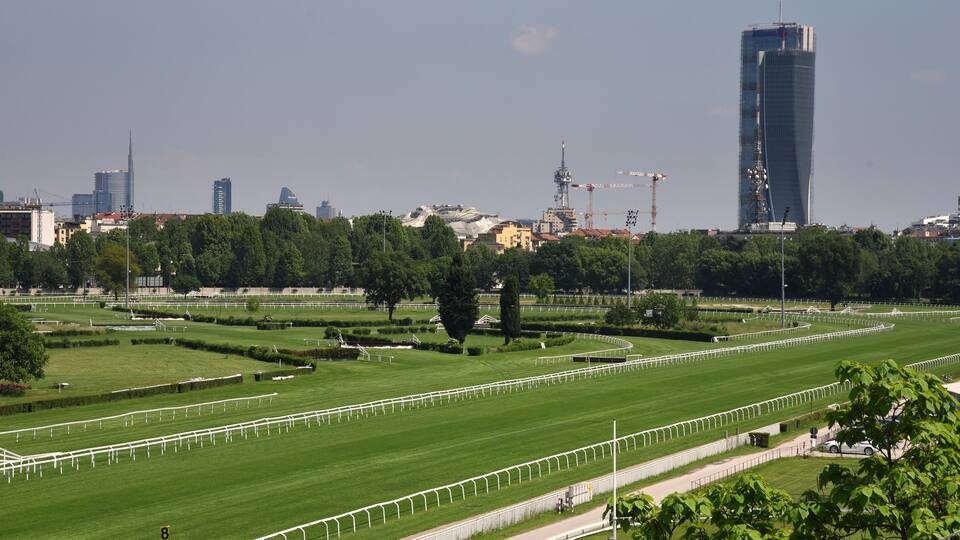 A large green park with white fences, trees, and a city skyline in the background.