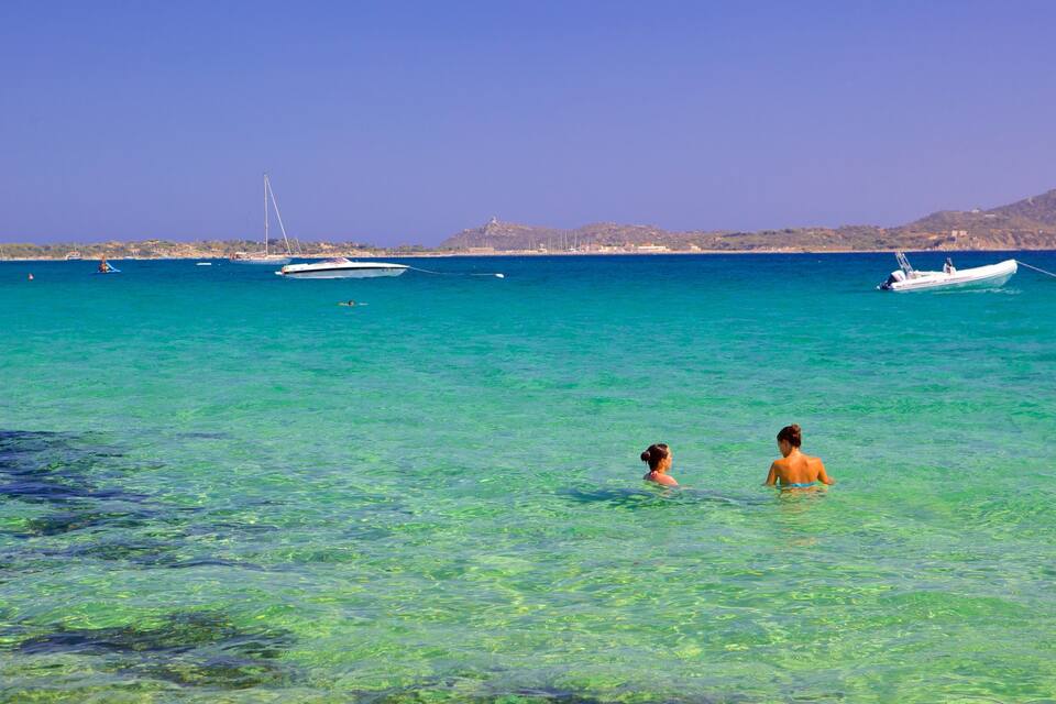 A clear turquoise sea with boats and a mountain in the background.