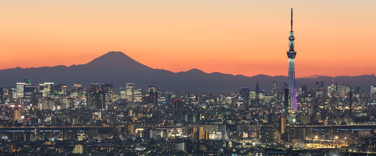 A cityscape at dusk with a prominent tower and a mountain in the background.