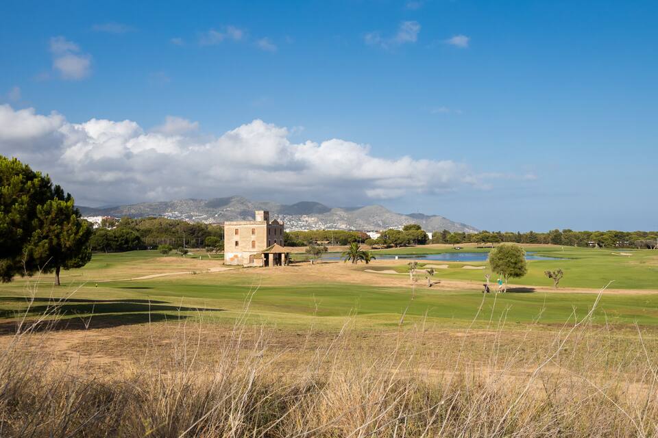 A golf course with a historic building, a lake, and mountains in the background.