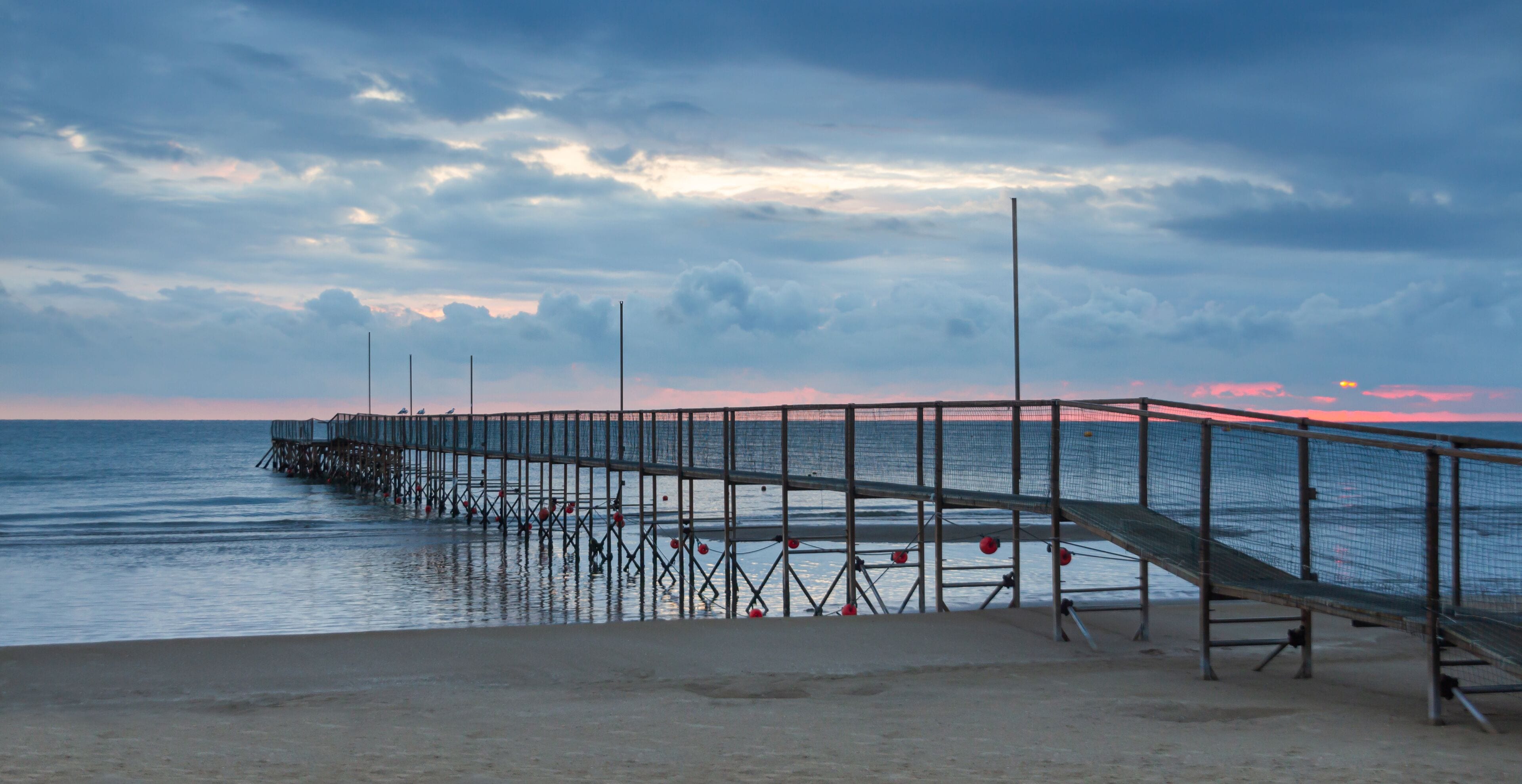 A pier extending into calm waters with a sunset in the background.
