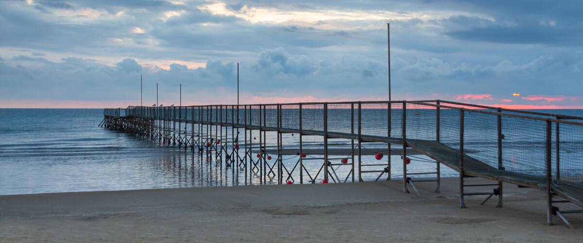 A pier extending into calm waters with a sunset in the background.