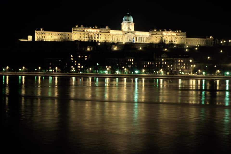 A large illuminated building with a dome, reflecting on a body of water at night.