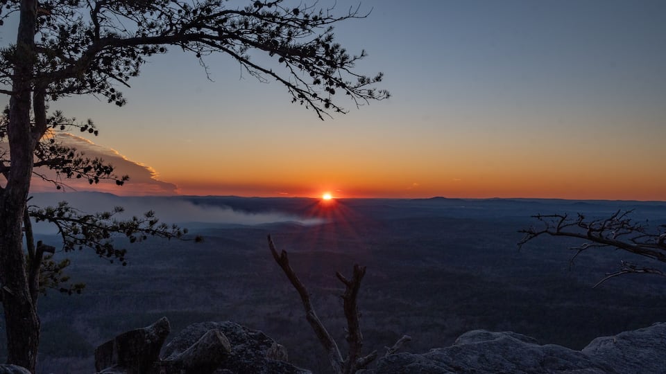 A sunset over a mountainous landscape with a tree in the foreground.