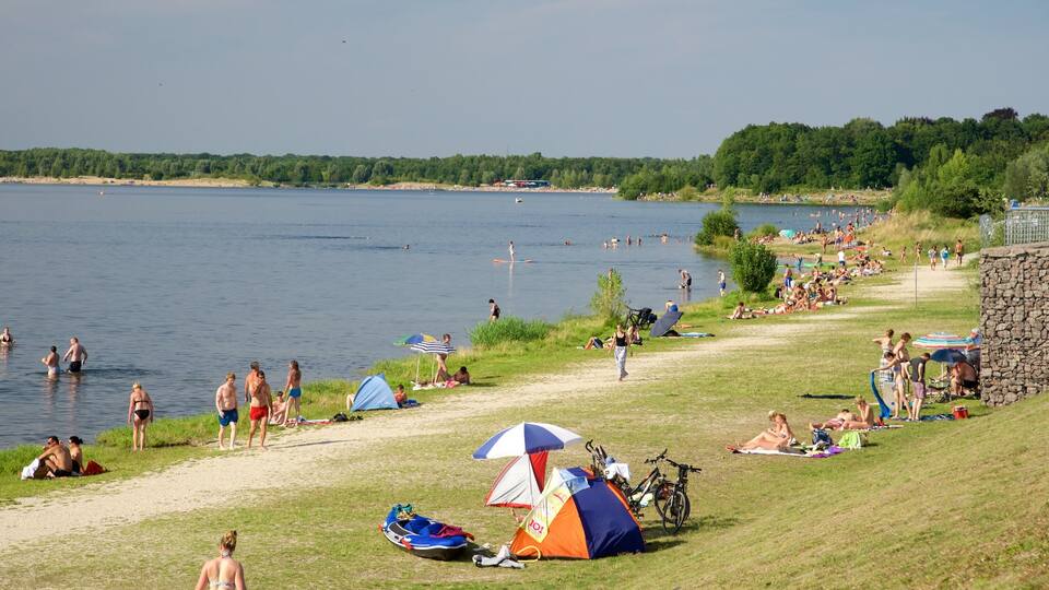 A lakeside beach with tents, people swimming, and a stone wall.