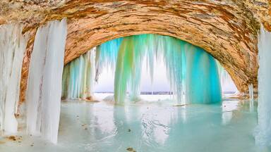 Giant ice cave with tall icicles of blue and green at entrance on lake