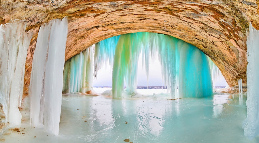 Giant ice cave with tall icicles of blue and green at entrance on lake