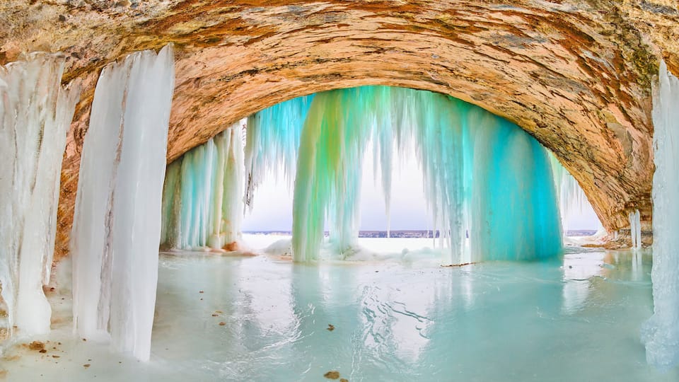 A cave with turquoise ice formations and a rocky ceiling.
