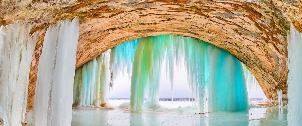 A cave with turquoise ice formations and a rocky ceiling.