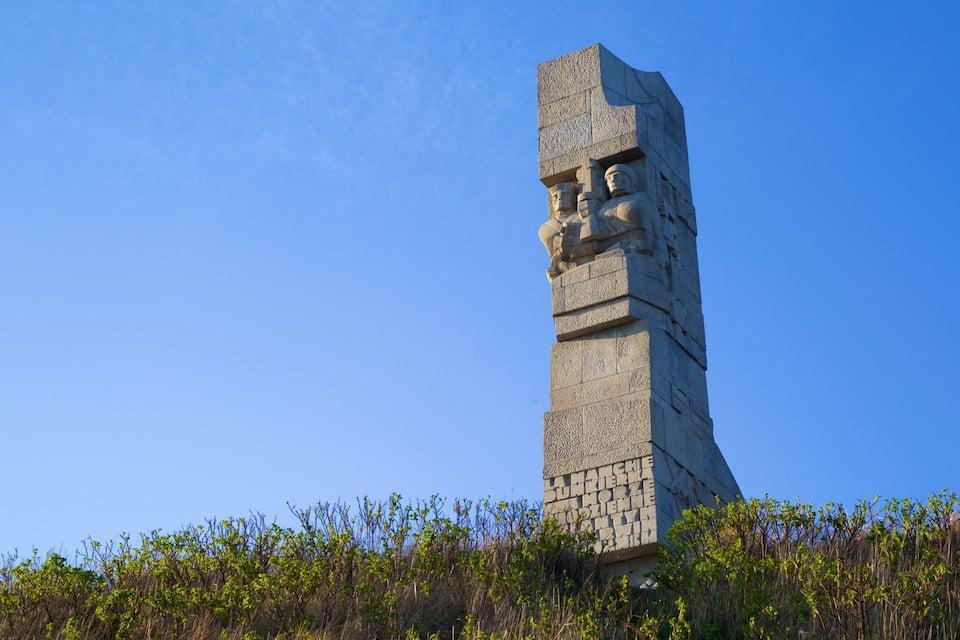 Un monumento de piedra alto con inscripciones, rodeado de follaje.