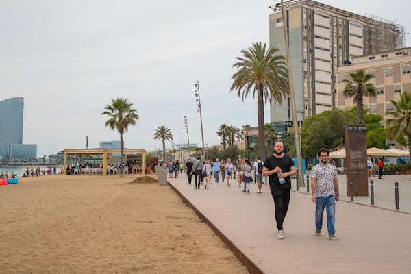 A beachside promenade with palm trees, a boardwalk, and a modern building in the background.