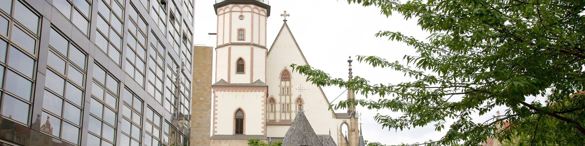 A historic church with a tall bell tower, surrounded by modern buildings and a public square with fountains and outdoor seating.
