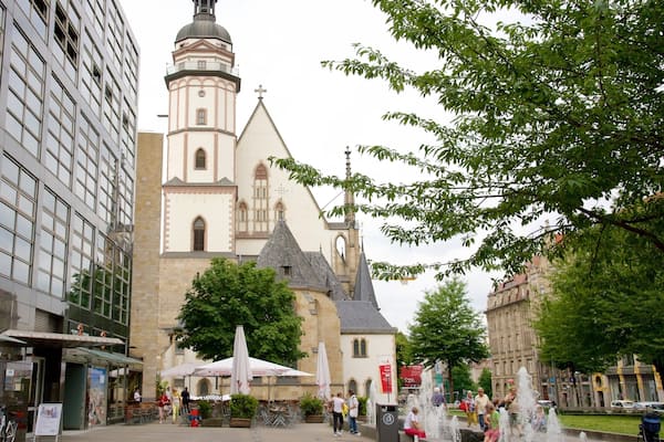 A historic church with a tall bell tower, surrounded by modern buildings and a public square with fountains and outdoor seating.