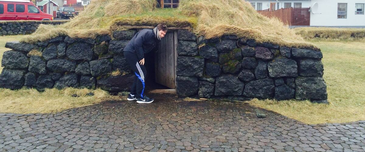 A person entering a traditional grass-roofed house with stone walls.