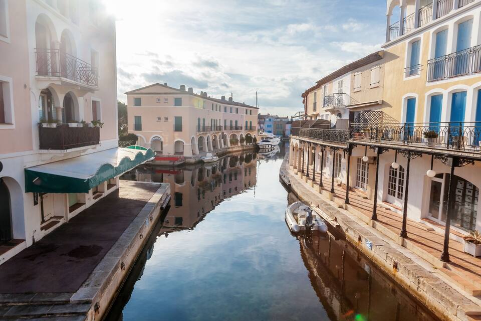 Um canal ladeado por edifícios, incluindo um prédio branco com toldo verde e um prédio amarelo com portas azuis.