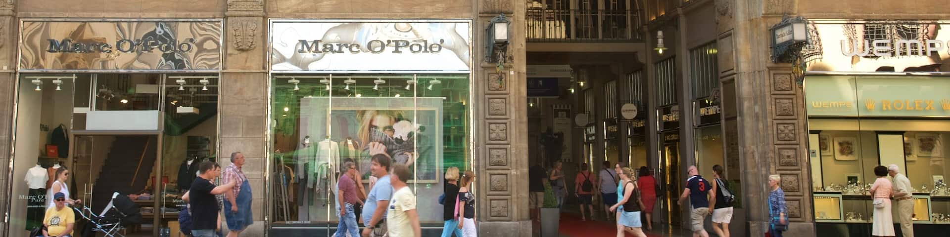A busy street with storefronts including Marc O'Polo and Rolex.