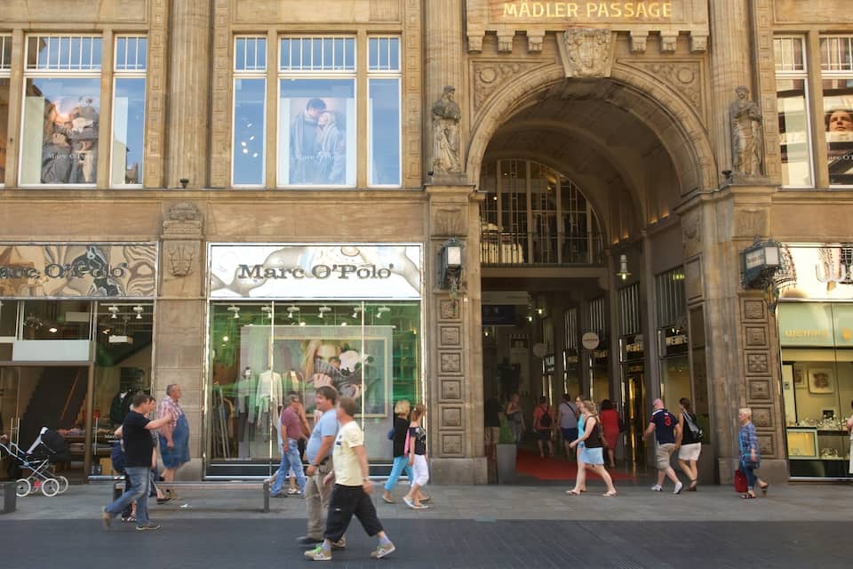A busy street with storefronts including Marc O'Polo and Rolex.