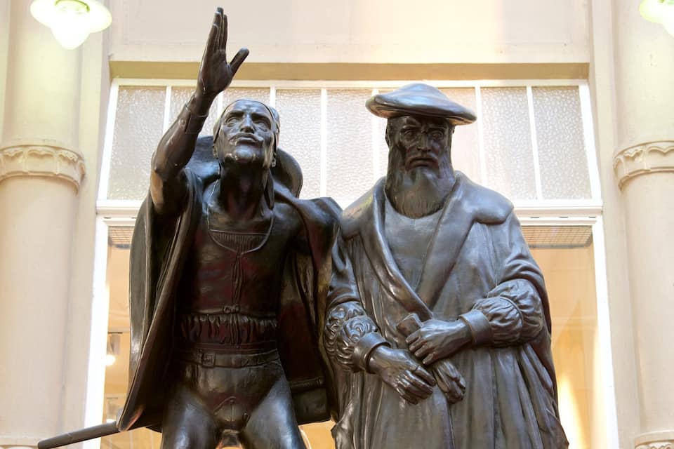 A statue of two figures, one with raised hand and the other with hands clasped.