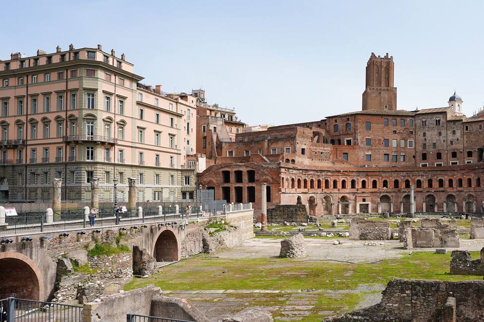 Um antigo anfiteatro romano com ruínas e edifícios modernos ao fundo.