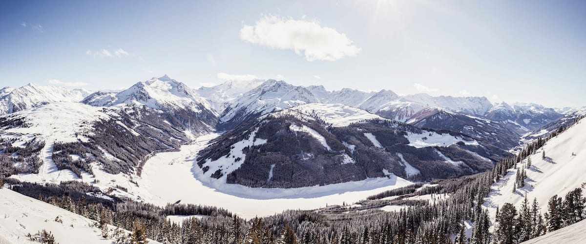 A snow-covered mountain range with a glacier and dense forests.