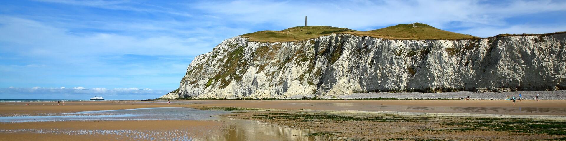 A coastal landscape with a prominent white cliff, a sandy beach, and a clear sky.