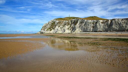 Un paysage cÎtier caractérisé par une falaise blanche imposante, une plage de sable et un ciel dégagé.