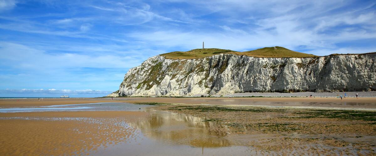 A coastal landscape with a prominent white cliff, a sandy beach, and a clear sky.